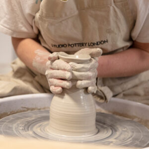 A close up of a potter with clay on the wheel making a vase